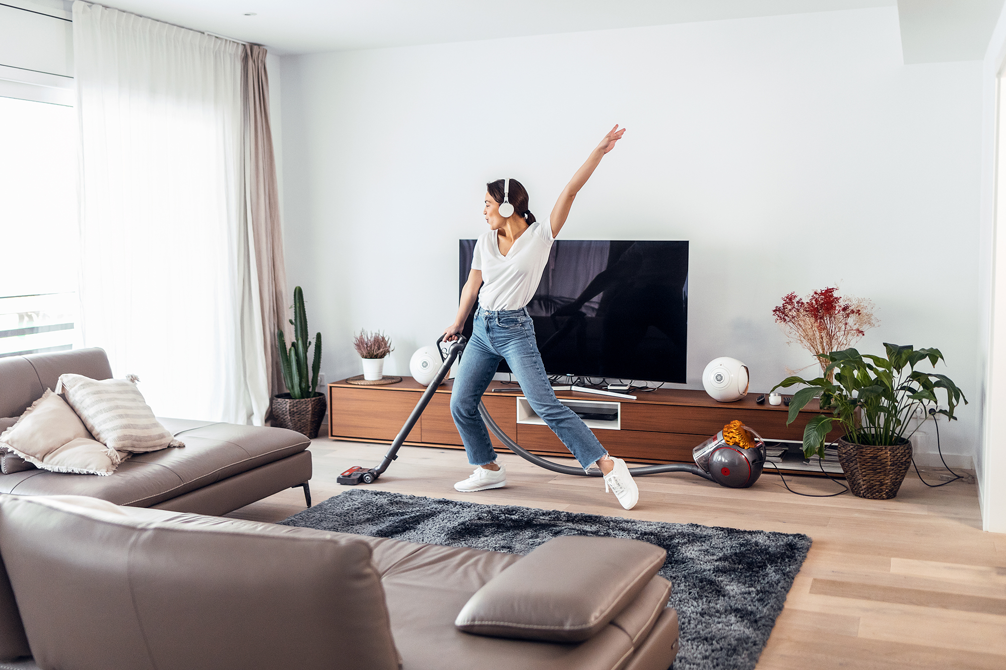 Young Happy Woman Listening And Dancing To Music While Cleaning The Living Room Floor With A Vaccum Cleaner